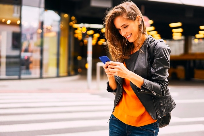 Mujer sonriente utilizando su teléfono celular en el exterior.